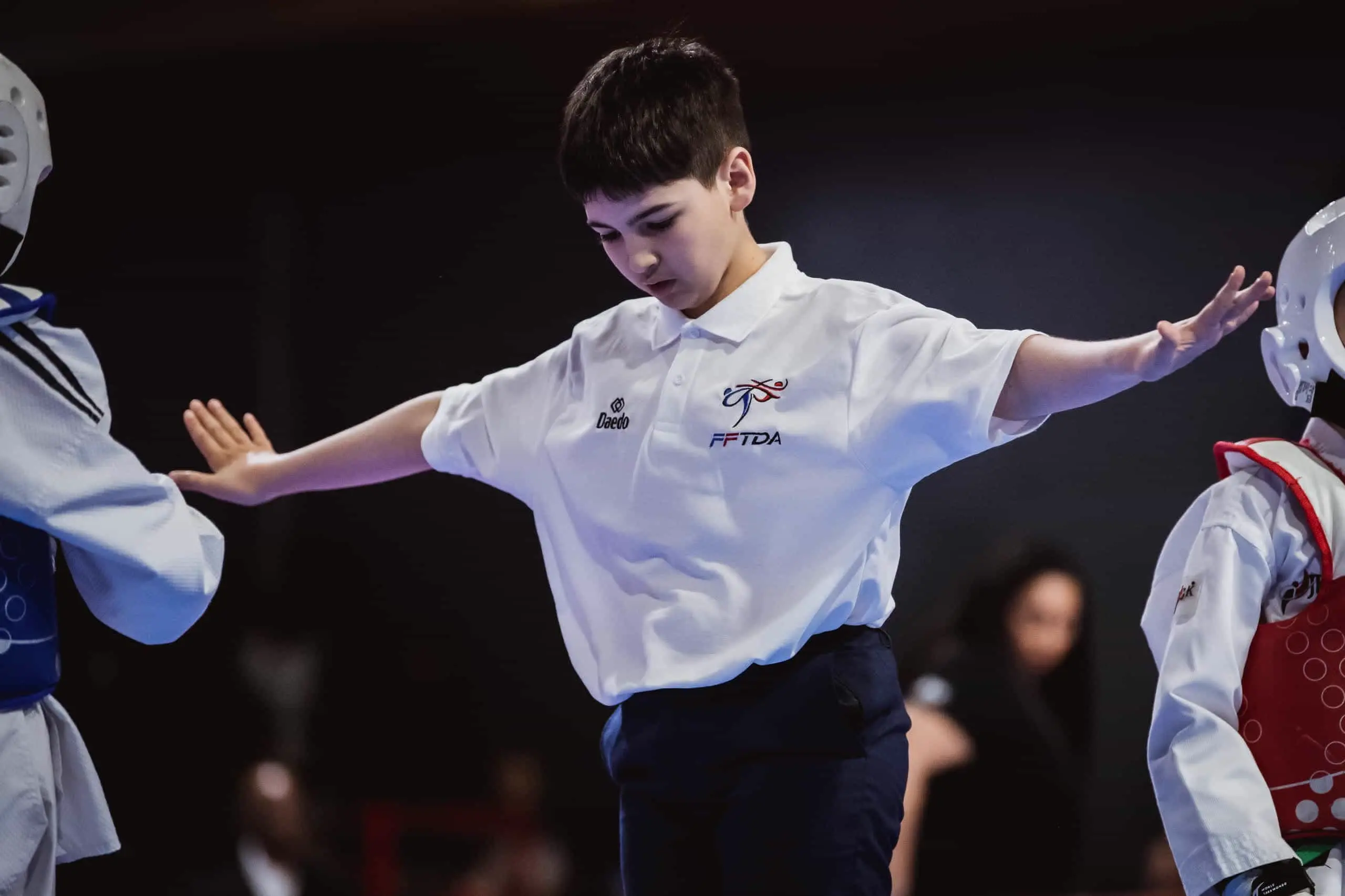 Un jeune arbitre en polo FFTDA sépare deux compétiteurs sur l'aire de combat.